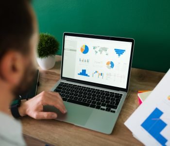 rear-view-young-man-working-his-laptop-looking-work-report-graphs-scaled